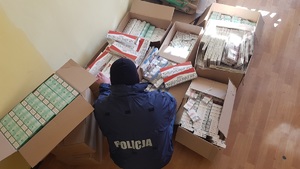 policjant oglądający kilka kartonów z paczkami papierosów