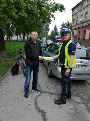 Policjant WRD wręcza pieszemu kamizelkę odblaskową.