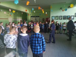Policjantka na szkolnym korytarzu edukuje dzieci o bezpiecznym spędzaniu wakacji.