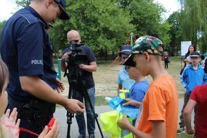 Policjanci wręczają dzieciom gadżety z logo kampanii &quot;Kręci mnie bezpieczeństwo nad wodą&quot;.