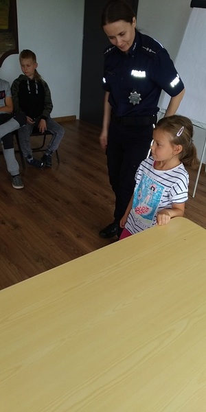 policjantka i dziewczynka stoją na tle innych dzieci