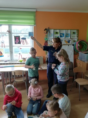 policjantka stoi pośród dzieci i prezentuje ulotkę