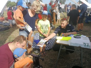 policjant wręcza edukacyjną kolorowankę dziecku w wózku. Obok rodzice i dwoje rodzeństwa dziecka w wózku