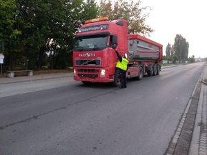 Samochód ciężarowy stoi ba drodze, a policjant sprawdza stan trzeźwości kierowcy.