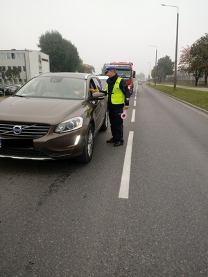 Policjant stoi przy samochodzie i podaje kierowcy alcoblow.