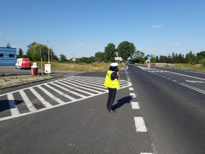 Umundurowana policjantka ruchu drogowego stoi przy drodze kontrolując ruch i mierząc prędkość ręcznym miernikiem.