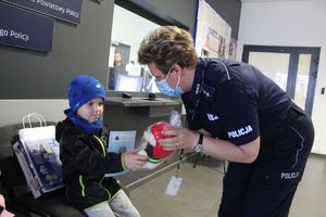 Policjantka wręcza książeczkę i maskotke misia małemu chłopcu