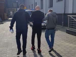 Policjanci prowadzą zatrzymanego męczyznę do radiowozu