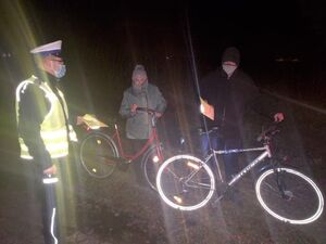 Policjant wręcza rowerzystom kamizelki odblaskowe