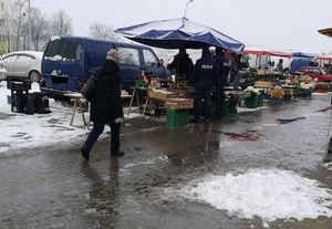 Dwaj policjanci stoją przy stanowisku targowym i dokonują sprawdzenia