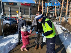 Policjant pochyla się nad dzieckiem i wręcza mu taśmę odblaskową