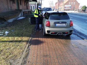 Policyjna kontrola drogowa. Umundurowany policjant stoi przy samochodzie, który zatrzymał się do kontroli.