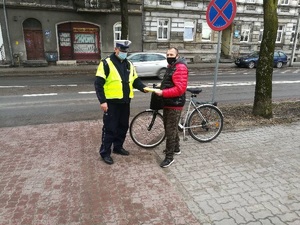 Policjant wręcza rowerzyście kamizelkę odblaskową