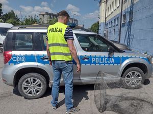 Policjant stoi przy radiowozie a przy nim sieci rybackie
