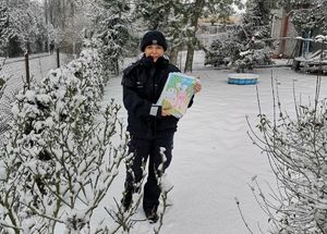 policjantka stoi w scenerii zimowej i trzyma w ręku prace rysunkowe  dzieci