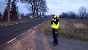 policjant ruchu drogowego stoi na poboczu i kontroluje prędkość pojazdów