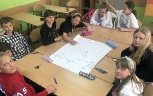 dzieci siedzą wokół kartki bristolu i piszą po niej