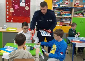 dzieci otrzymują od policjanta elementy odblaskowe