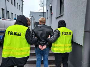 policjanci prowadzą mężczyznę który ma ręce w kajdankach