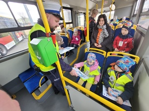 policjant rozdaje dzieciom w autobusie policyjne ulotki