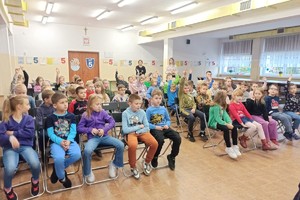 Opiekunowie oraz dzieci podnoszące dłonie.
