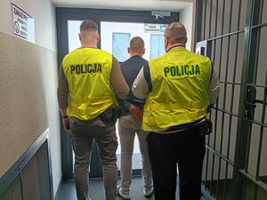 Dwóch policjantów trzyma zatrzymanego.