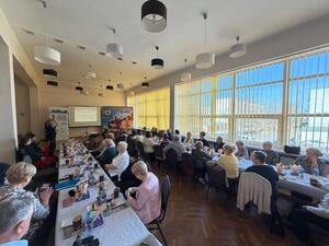 seniorzy siedzą przy stole słuchając prelekcji policjantki