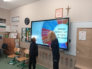 policjantka z uczniem stoi przy tablicy multimedialnej i kręcą multimedialnym kołem