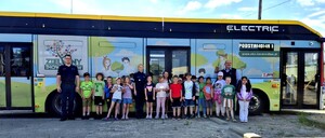 Dzieci z policjantami pozują do zdjęcia na tle autobusu miejskiego.