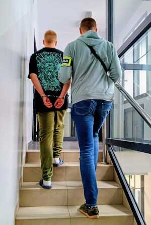 Policjant prowadzi po schodach zatrzymanego.